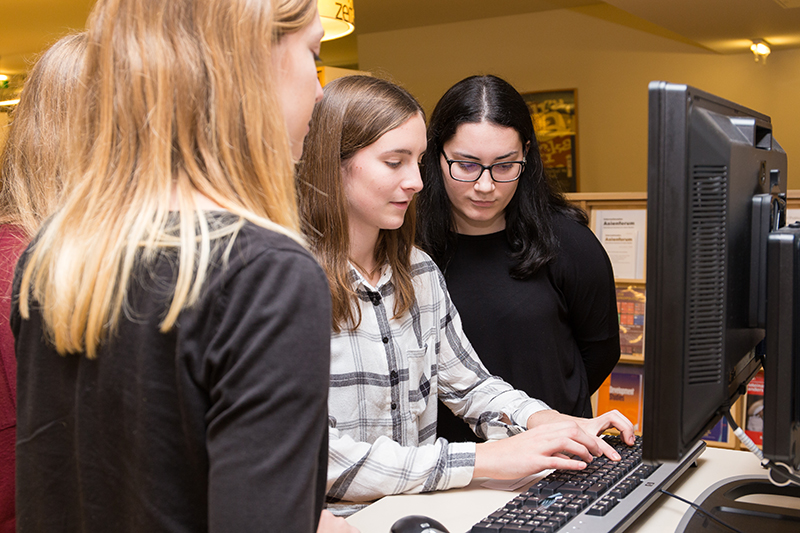 3 junge Frauen vor einem PC, eine tippt