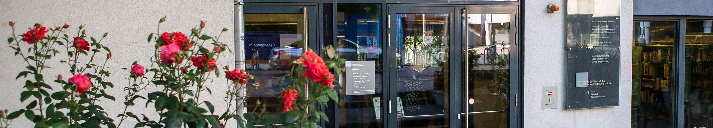 Zu sehen ist der Eingang in die C3 Bibliothek. Links im Eck sind Rosen, die vor dem Gebäude wachsen.